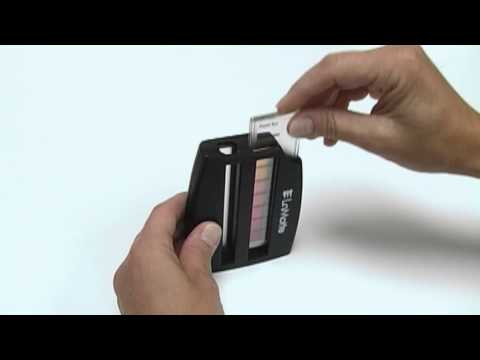 A person uses a Phosphate Test Kit - 4401-02, sliding a sample strip into the color comparator to compare its hue against reference color bars.