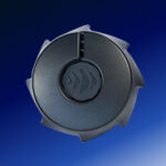 A round, dark gray plastic object with four notched edges and a central circular design, set against a blue gradient background.